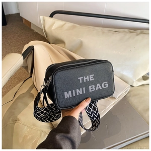 Detail of black pebbled leather mini camera bag with grey lettering and geometric strap
