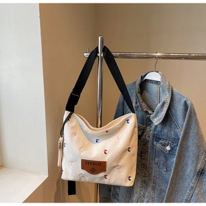 Detail of white canvas bucket bag featuring colorful embroidery and wide black strap