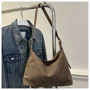 Close-up of large brown suede tote bag hanging on metal rack with denim jacket accent