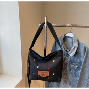 Detail of black canvas tote featuring colorful letter embroidery and brown leather patch
