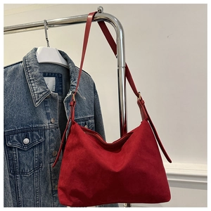 Detail of red suede hobo shoulder bag with metal buckle hanging next to denim jacket