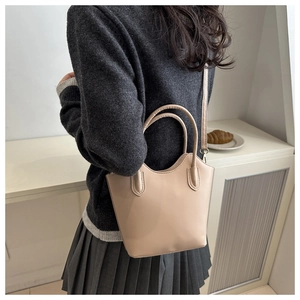 Close-up of beige minimalist bucket bag with dual handles and slender shoulder strap
