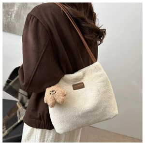 Detail of plush off-white tote bag with brown leather strap and teddy bear charm