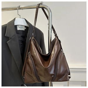 Detail of dark brown faux leather hobo bag with decorative side zippers on black background