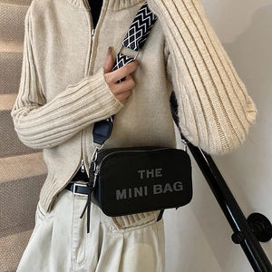 Minimalist black pebble leather camera bag with THE MINI BAG print and woven strap