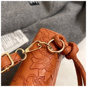 Détail d'un sac en cuir gaufré marron avec motifs floraux et ferrures dorées