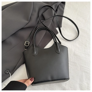Detail of a black bucket bag with dual handles and adjustable strap on textured fabric