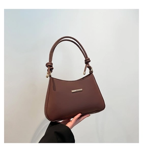 Close-up of brown leather shoulder bag featuring gold metal bar and knotted strap detail
