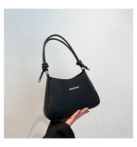 Detail view of black faux leather handbag featuring golden metal bar and knotted strap