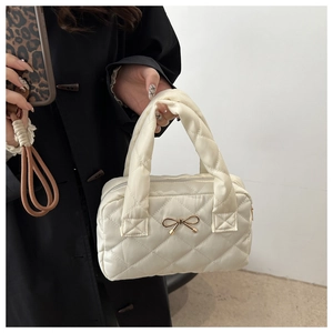 Detail of a beige quilted tote bag with a golden metal bow and elegant diamond pattern