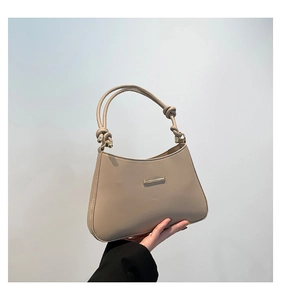 Detail of beige faux leather shoulder bag featuring gold hardware and knotted strap handles