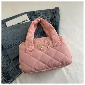 Close-up of pink quilted bag with gold bow on denim jacket and white book background