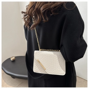Détail du petit sac carré crème avec motif crocodile et bandoulière chaîne dorée
