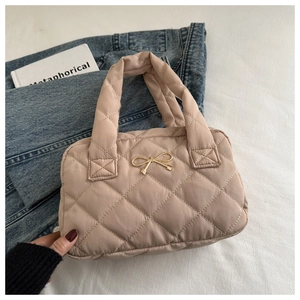 Detailed close-up of quilted cotton tote bag with golden bow clasp on beige fabric