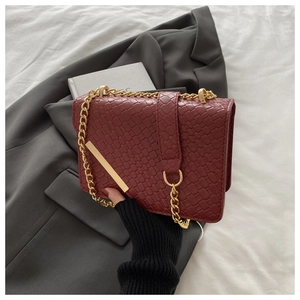 Gros plan d'un sac bandoulière rouge texturé avec chaîne dorée et boucle métallique