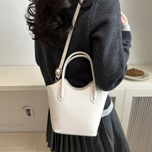Minimalist beige bucket bag with top handles and crossbody strap on an elegant model