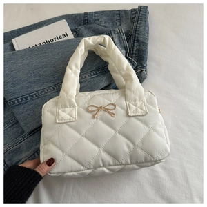 Detail of cream quilted handbag with elegant gold bow clasp and rounded top handle