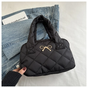 Macro view of black quilted nylon handbag featuring a golden metal bow and diamond pattern