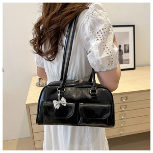 Detail of glossy black shoulder bag with double front pockets and silver bow charm