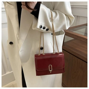 Close-up of a red patent leather crossbody bag with a gold metal clasp and chain strap