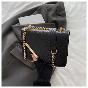 Détail du sac bandoulière noir tissé avec chaîne dorée posé sur un blazer gris