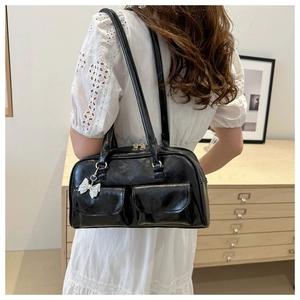 Detail of glossy black leather handbag featuring dual front pockets and silver bow charm