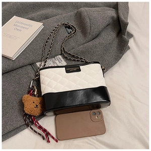 Détail du sac bandoulière matelassé bicolore avec chaîne et pendentif ours en peluche