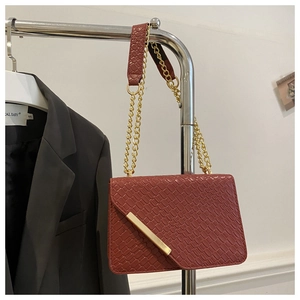 Détail du sac marron rouge à motif crocodile avec rabat asymétrique et barre en métal doré