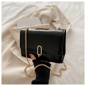 Detail of black glossy crossbody bag with gold chunky chain strap and metal clasp lock
