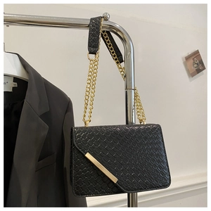 Détail d'un sac en cuir de crocodile noir avec barre métallique dorée et bandoulière chaîne