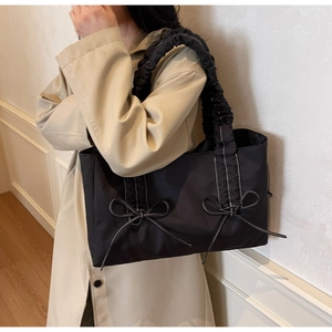 Détail du cabas noir avec nœud et anses froncées porté par un mannequin en trench beige
