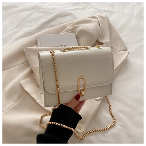 Close-up of cream square bag with gold oval lock and chain strap on beige blazer