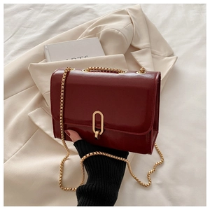 Detail view of burgundy crossbody bag with gold metal lock and chain on elegant background