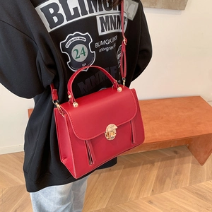 Elegant red square handbag with gold lock and shoulder strap worn by a model in casual style