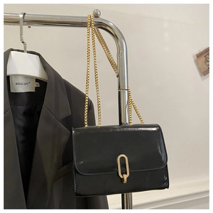 Detail of black glossy leather crossbody bag with gold chain and metal lock