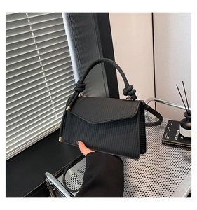 Detail of black woven texture square bag with knotted handle and envelope flap design