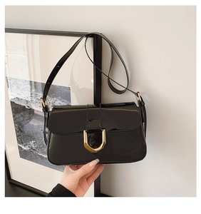 Detail of glossy patent leather handbag with gold horseshoe buckle and adjustable strap