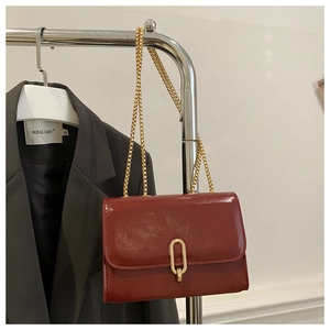 Detailed macro of burgundy patent leather bag featuring a gold metal buckle and chain
