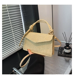 Close-up of beige woven crossbody bag featuring a twisted ring handle and gold hardware