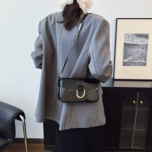 Minimalist black patent leather shoulder bag with gold horseshoe buckle on model back