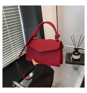 Detail view of the red woven handbag showing the textured knot handle and flap closure