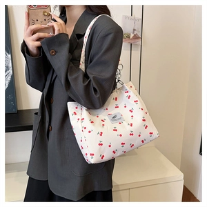 Close-up of white tote bag with red cherry pattern and blue square fabric label detail