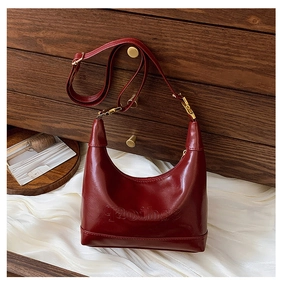 Close-up of vintage dark red leather pillow bag with elegant gold hardware on wood