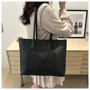 Detail of black tote bag with snake embossed texture panel and matte smooth sides