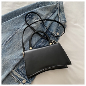 Detail shot of black crossbody bag with curved base and gold hardware on denim jacket