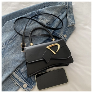 Detail of black matte leather handbag with gold D-buckle and curved base on white fabric