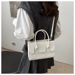 Close-up of a white leather crossbody bag with pointed flap design and gold hardware