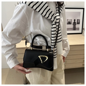 Detail of black glossy leather handbag with curved base and gold D-ring buckle accessory