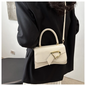 Detailed view of cream leather crossbody bag featuring a large gold D-shaped buckle