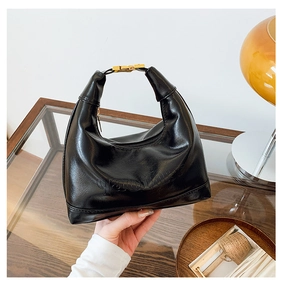 Detail view of black patent leather hobo bag with embossed lettering on glass table